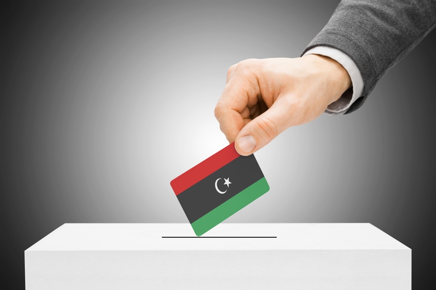 A hand inserting a Libyan flag into a ballot box