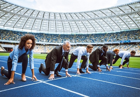 Executives of different ages and color standing at the starting line in a stadium about to begin a race.