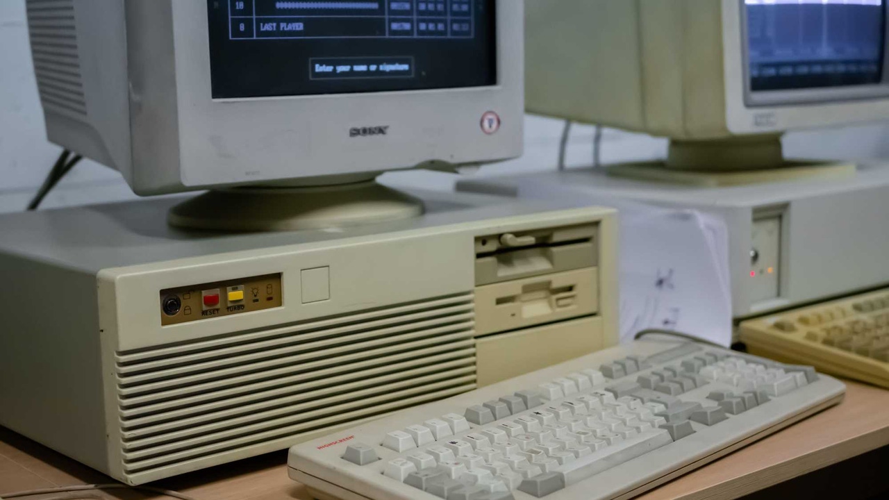 Two old-school desktops with floppy drives and a keyboard on a desk. Two old-school desktops with floppy drives and a keyboard on a desk.
