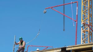 Construction workers wearing safety harnesses attached to an Alsina Fall Arrest System work against a clear blue sky