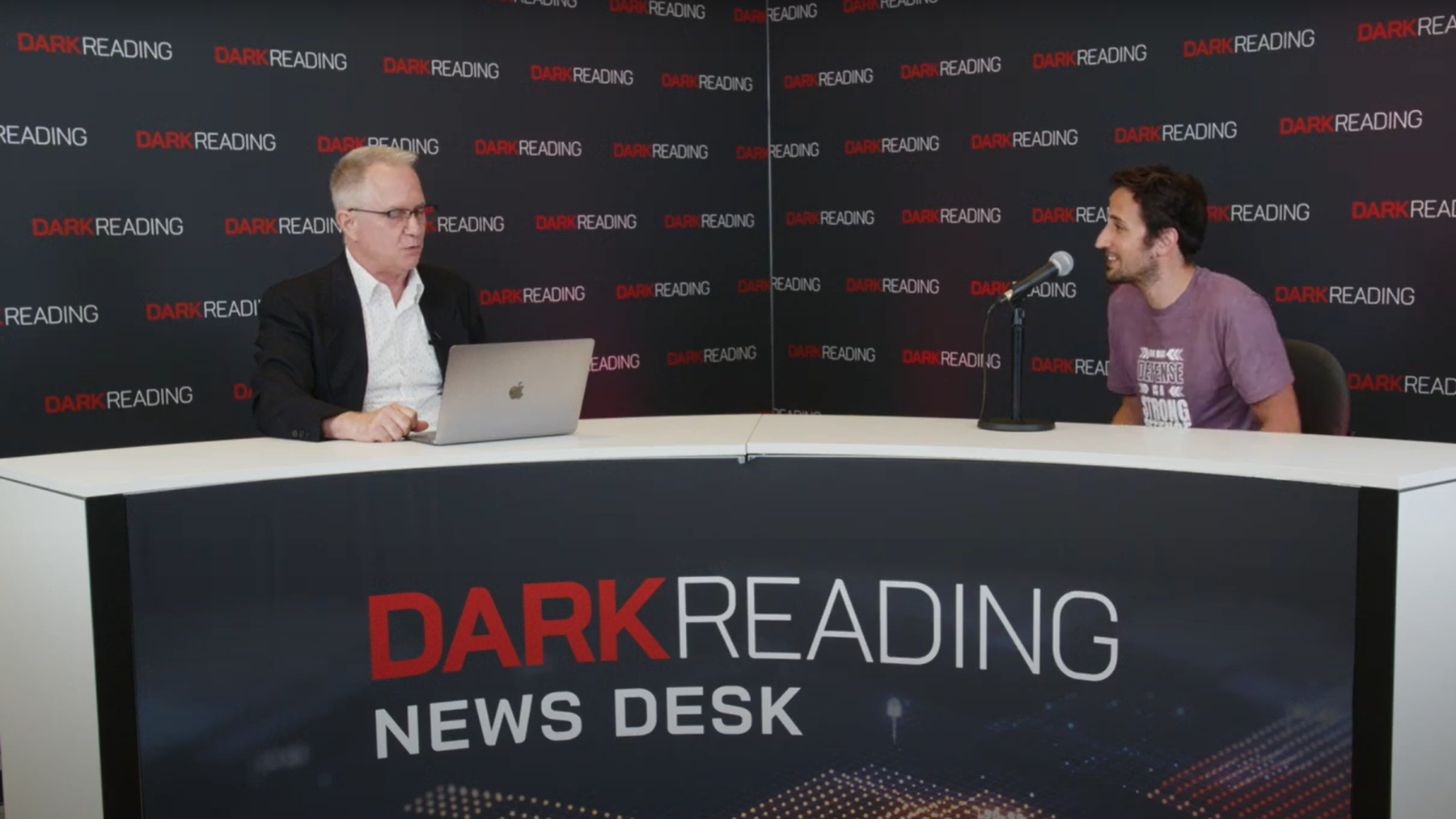 Two people talking at a news desk against a dark backdrop with "Dark Reading" written on it.