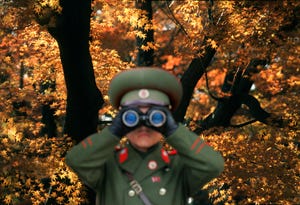 North Korean soldier looking through binoculars against autumn tree
