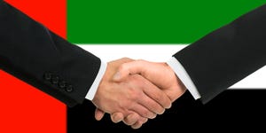 Two men shaking hands in front of the UAE flag