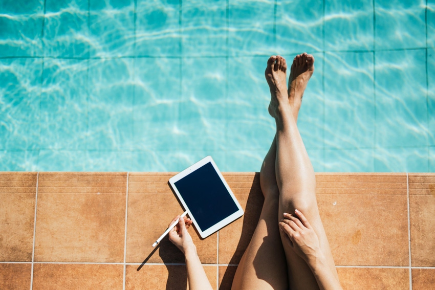 Woman on tablet with legs over a hotel pool