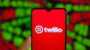 A person's hand holding a phone with the Twilio logo on the screen in white on a red background A person's hand holding a phone with the Twilio logo on the screen in white on a red background