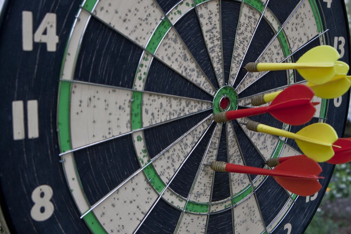 Image of darts target with six arrows hanging on red wooden wall.