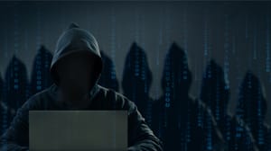 A hooded figure sitting in front of laptop A hooded figure sitting in front of laptop