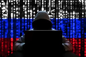 A hooded figure with a laptop in front of a coded background in the colors of the Russian flag