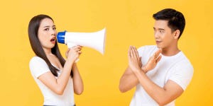 Asian-looking female making an announcement with a bullhorn and an Asian-looking male reacting negatively with crossed arms..