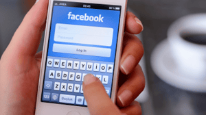 Hands holding a white mobile device showing the Facebook login page Hands holding a white mobile device showing the Facebook login page