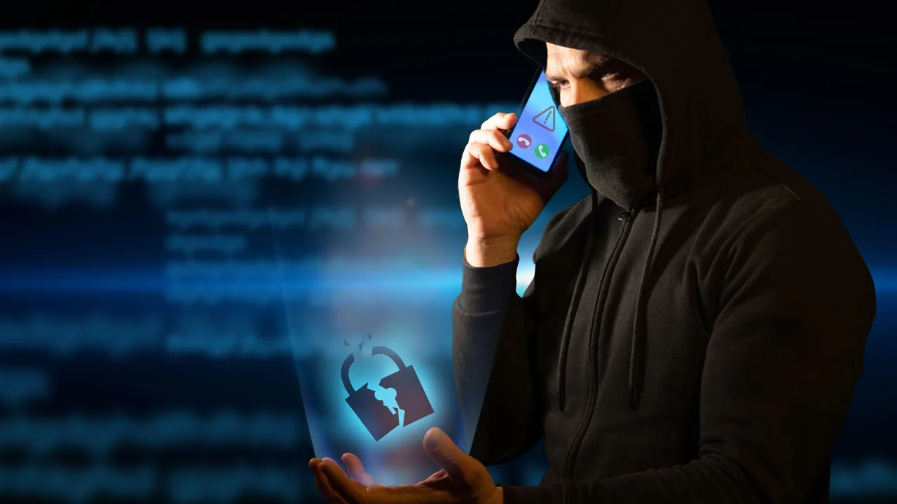 フード付きスウェットとマスクを着けた人物が携帯電話を耳に当て、開いた手から壊れた南京錠の画像が伸びている フード付きスウェットとマスクを着けた人物が携帯電話を耳に当て、開いた手から壊れた南京錠の画像が伸びている