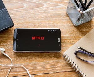 A photo of a desk with a mobile phone showing the Netflix logo.