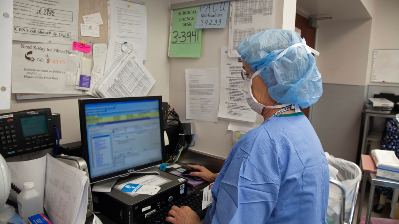 Nurse in blue scrubs enters data into computer Nurse in blue scrubs enters data into computer