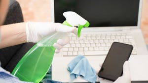Close up of a person cleaning and sanitizing tech devices such as laptop and mobile device.