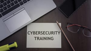 An image of desk with a laptop, phone, glasses, and pencil with card labeled "Cybersecurity training." An image of desk with a laptop, phone, glasses, and pencil with card labeled "Cybersecurity training."