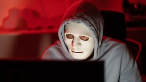 Computer hacker wearing white mask stealing data from a laptop Computer hacker wearing white mask stealing data from a laptop