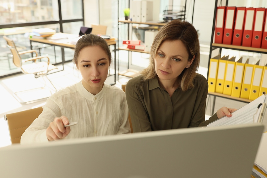 Photo of two women doing work on a big monitor in an office