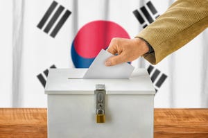 Hand putting a ballot in a ballot box in front of a Korean flag
