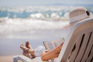Photo of a person reading a book on the beach.