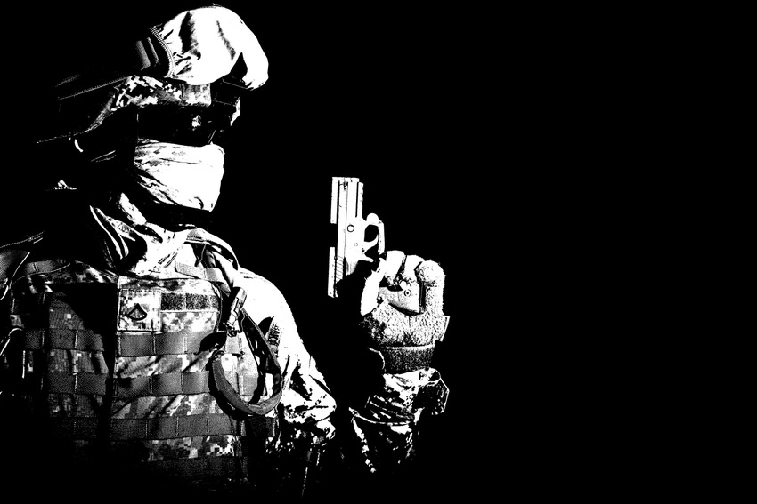 A black and white photo of a soldier with a full face covering holding a pistol