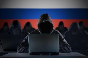 A group of hooded figures with laptops in front of the Russian flag