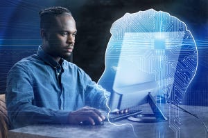 Businessman with cornrows uses desktop computer with the implied assistance of AI, represented as a glowing circuitboard head