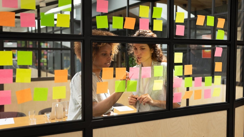 Two women strategizing in front of a wall of Post-it notes