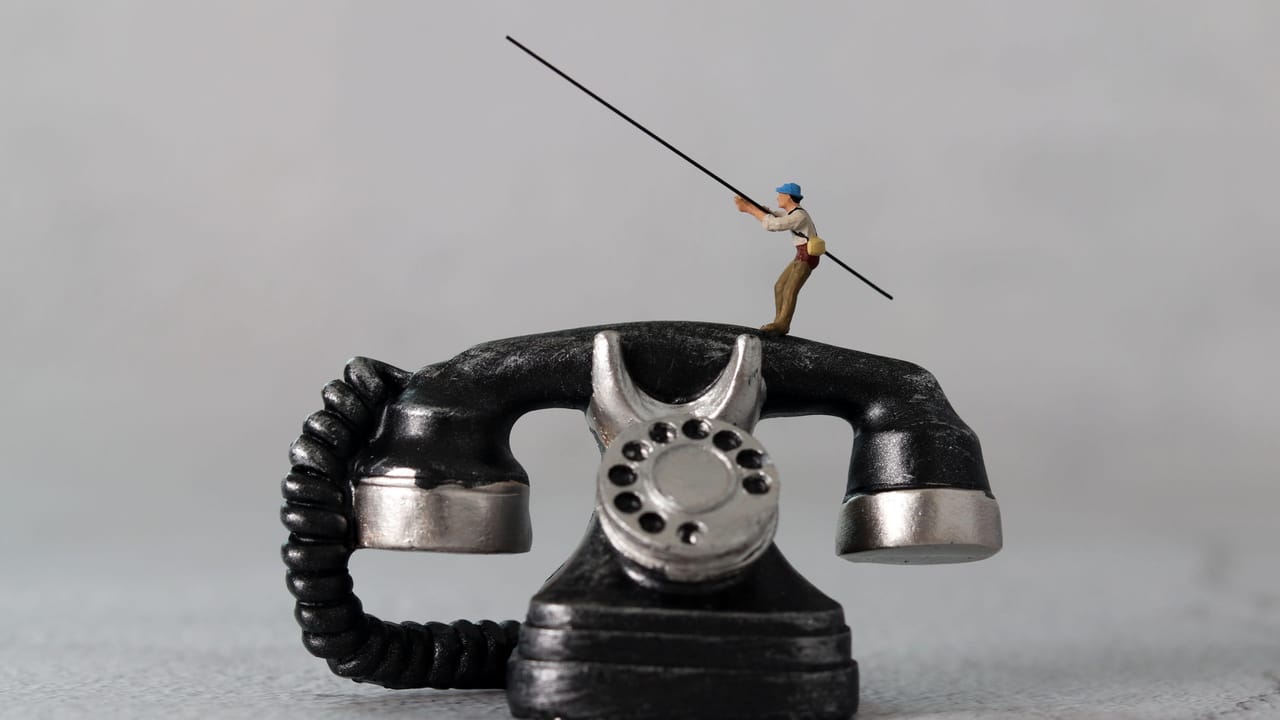 A tiny figurine of a fisherman holding a fishing rod on top of a rotary dial telephone A tiny figurine of a fisherman holding a fishing rod on top of a rotary dial telephone