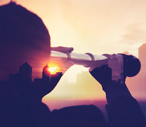 Silhouette of a person looking through binoculars into the distance, during sunset.