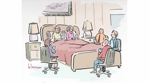 A group of people holding devices sitting around a bed. A group of people holding devices sitting around a bed.