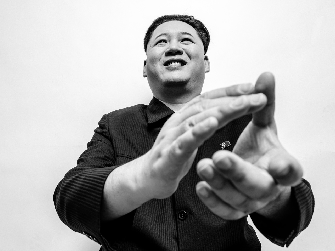 Image shows a dark-haired man of Asian descent in a suit with his hands in front of him appearing to clap Image shows a dark-haired man of Asian descent in a suit with his hands in front of him appearing to clap