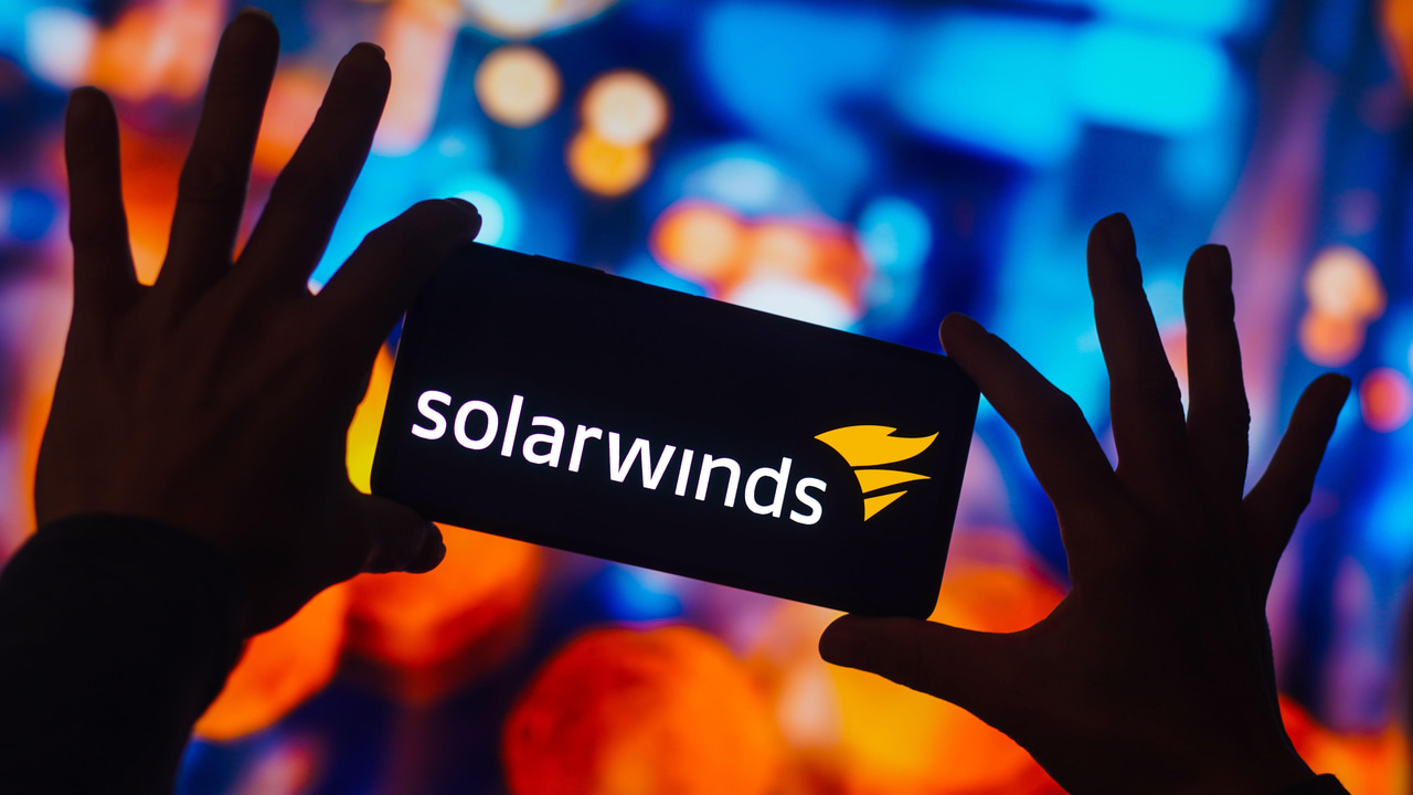 The silhouette of a person's hands holding a phone with the SolarWinds logo on the screen; bright, blurred colors in the background The silhouette of a person's hands holding a phone with the SolarWinds logo on the screen; bright, blurred colors in the background