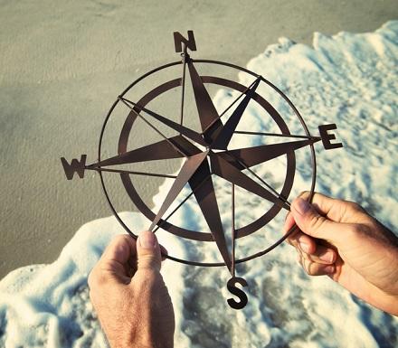 Hands holding simple metal compass rose outdoors on the shore of an empty beach with crashing waves