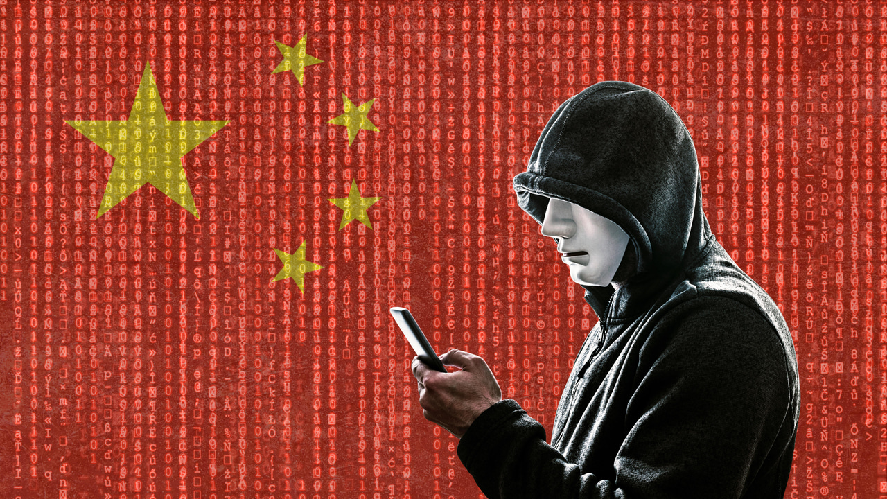 A person in a hoodie, holding a phone, in front of a Chinese flag A person in a hoodie, holding a phone, in front of a Chinese flag
