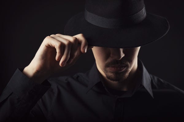 man wearing and tipping a black hat, depicting a hacker man wearing and tipping a black hat, depicting a hacker