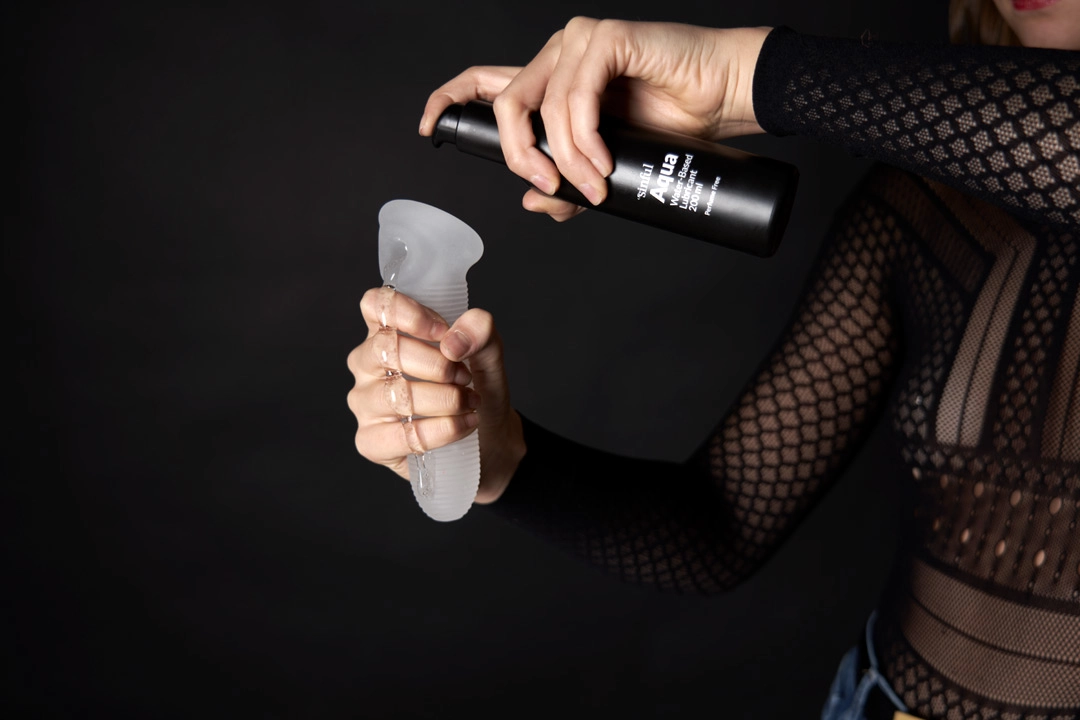 En hånd holder et penis sleeve og en anden pumper glidecreme på det