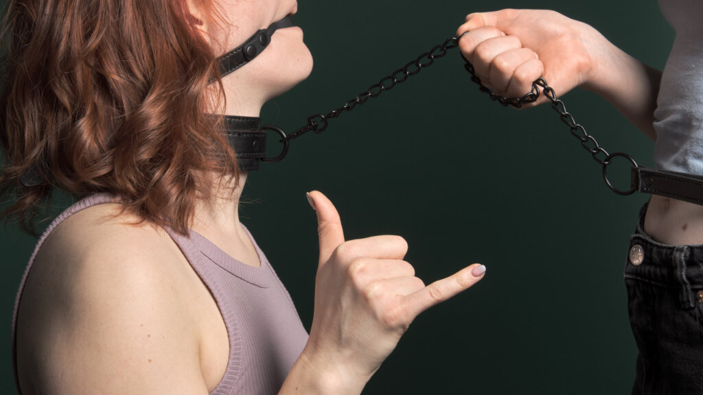 Woman with ball gag and collar showing a sign with her hands