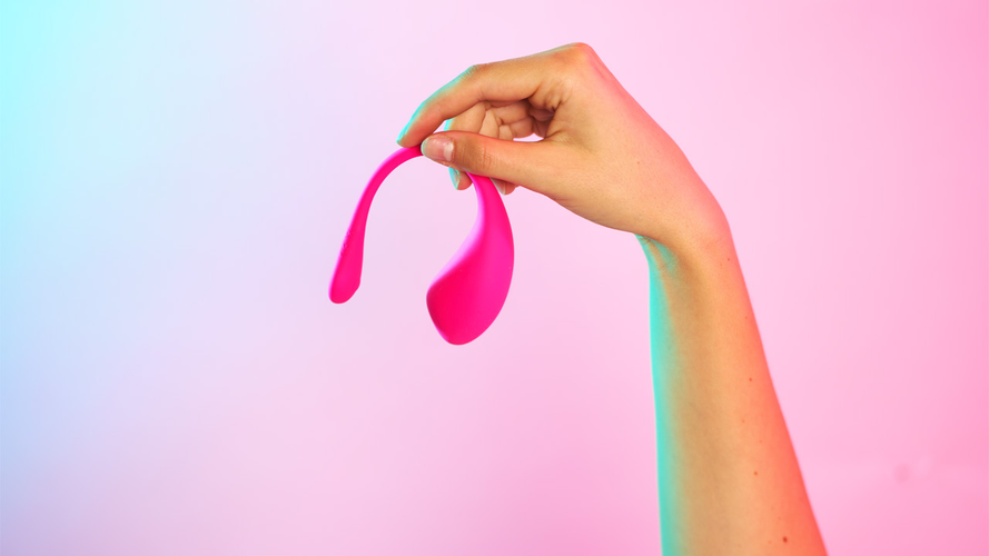 Een hand die een Lovense Lush 3 vasthoudt voor een roze achtergrond