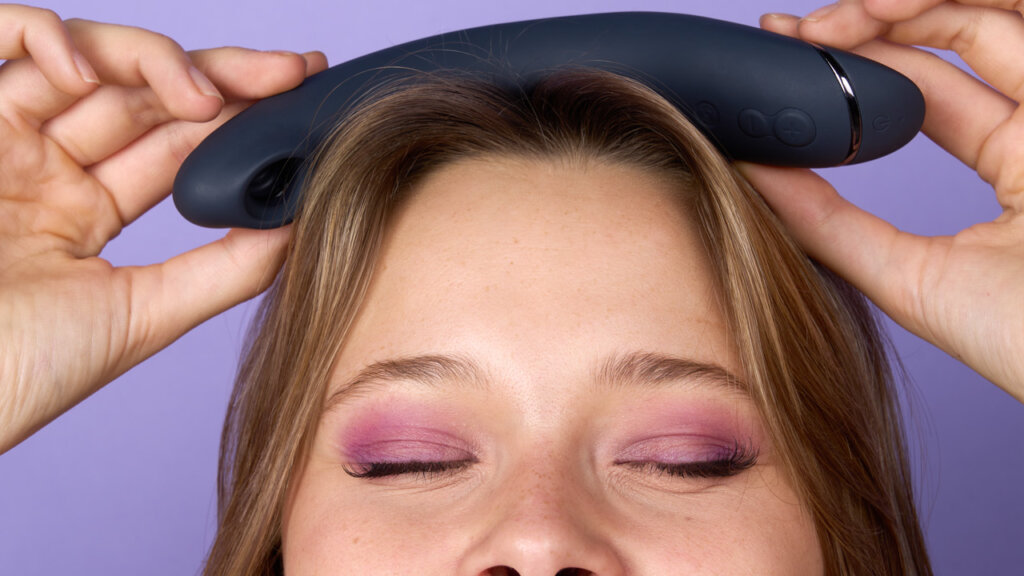 Nærbilde av en person med rosa øyenskygge som holder et blått sexleketøy oppå hodet