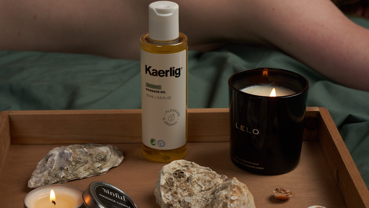 Beleuchtete Massagekerzen und ein Massageöl stehen in einer Holzkiste
