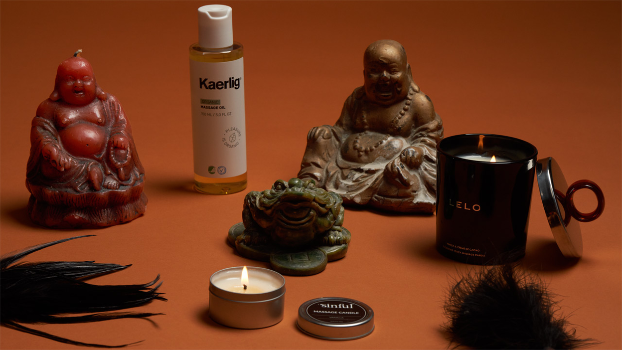 Bougies de massage Lelo et Sinful allumées, huile de massage Kaerlig et figures de Bouddha sur fond orange