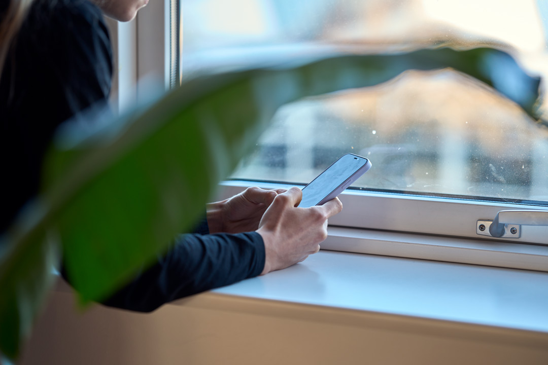 Eine Person sitzt vor einem Fenster und schreibt eine SMS