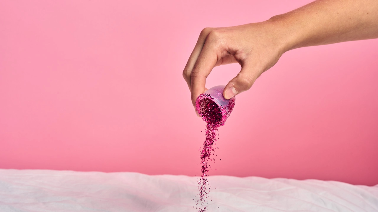 Eine Hand schüttet Glitter aus einer Menstruationstasse heraus