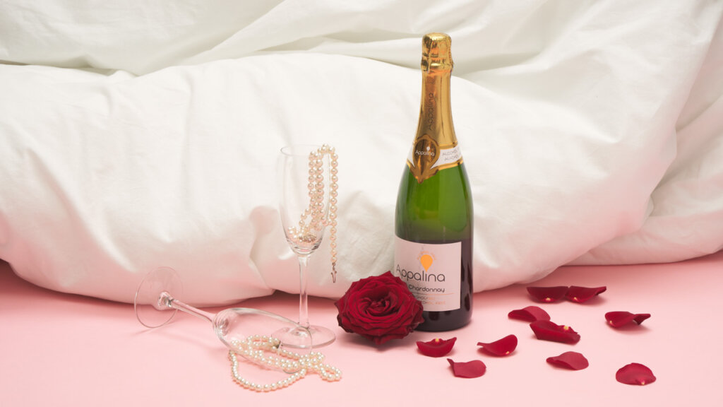 To glass, en flaske med champagne, en rød rose og mange roseblad