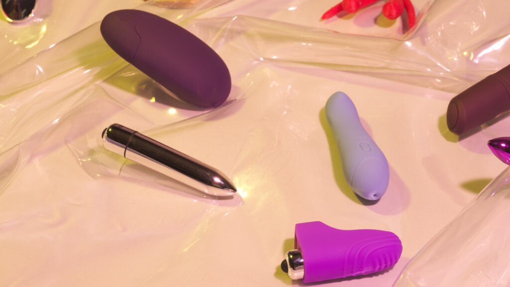Et udvalg af klitoris vibratorer ligger på gennemsigtigt plastik på en beige baggrund
