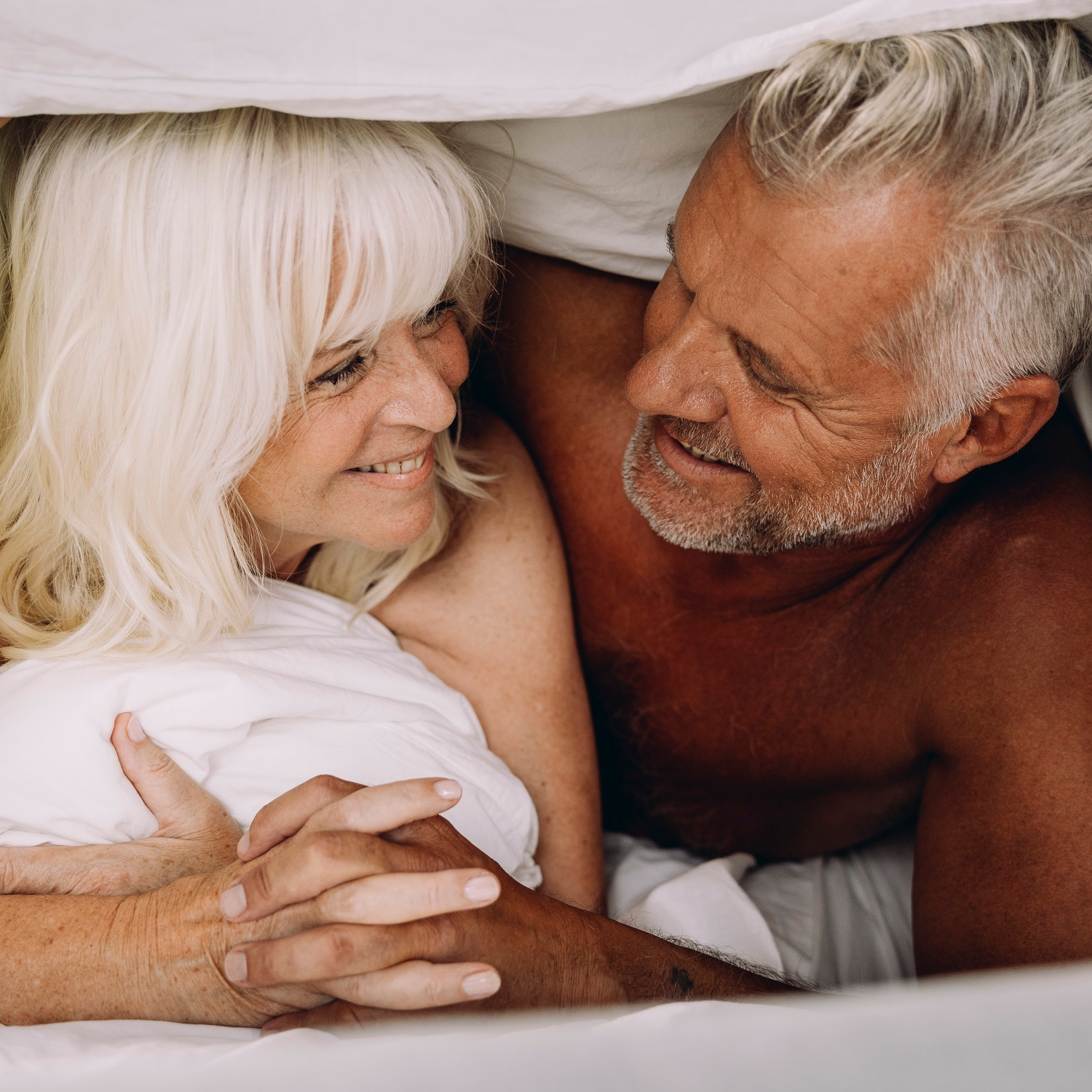 Two elderly people lie in bed and laugh at each other