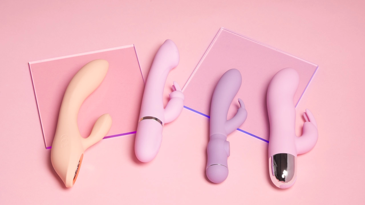 Fire rabbitvibratorer i lyse farger som ligger ved siden av hverandre på en rosa bakgrunn