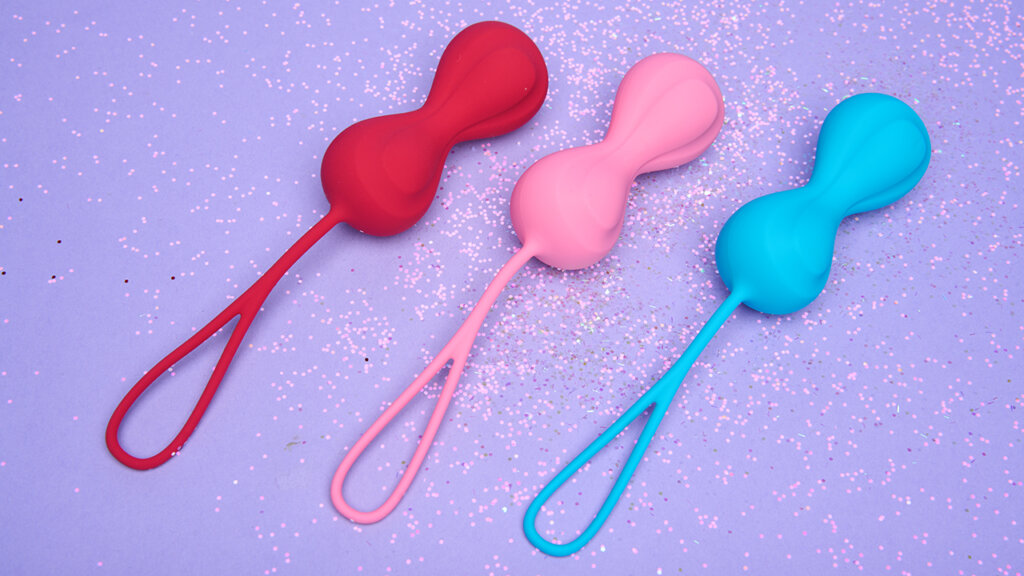 Three kegel balls in different colours on a light purple background with glitter