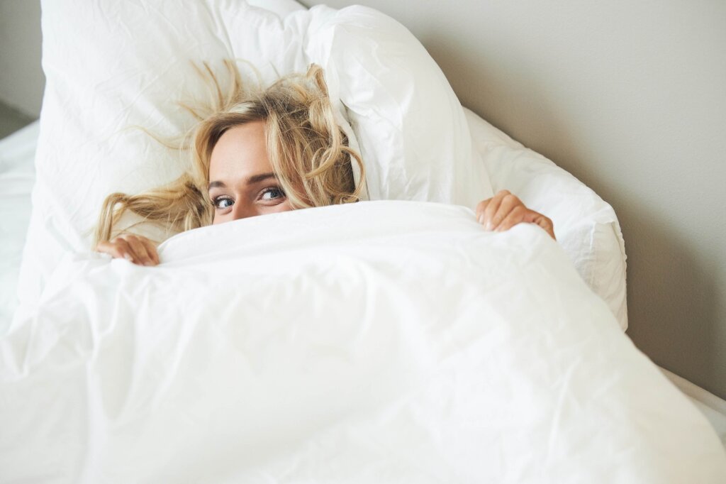 Kvinde kigger frem under en dyne i en seng
