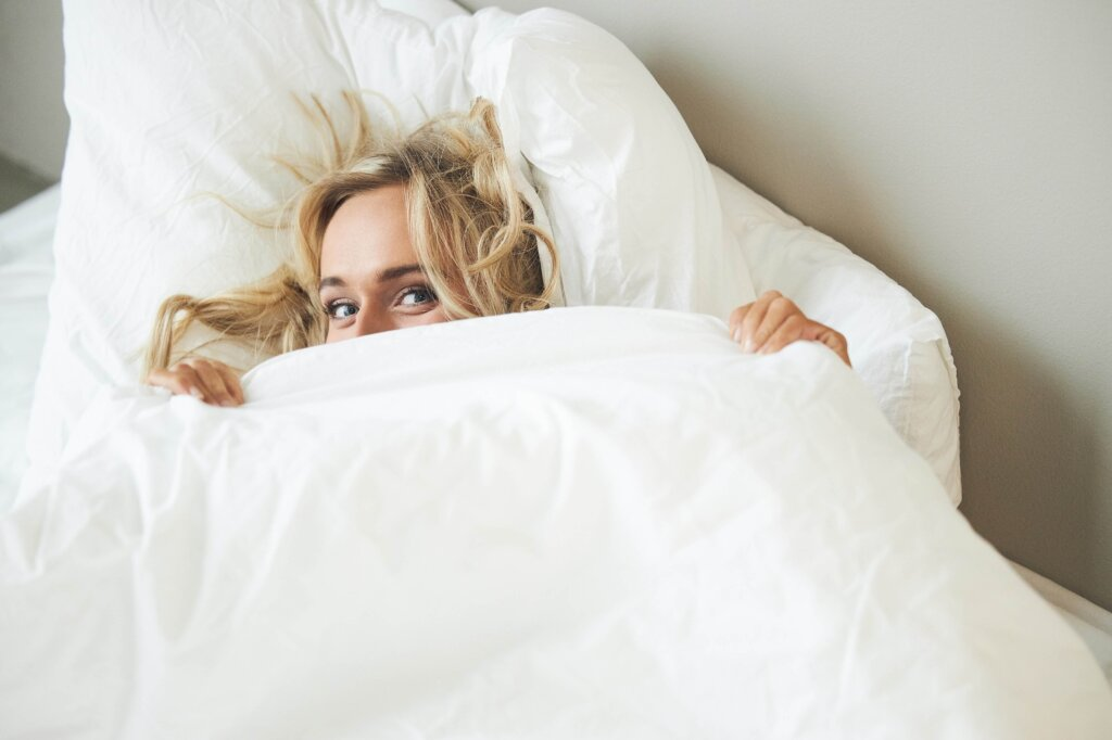 Fair-haired woman looks out from under a duvet